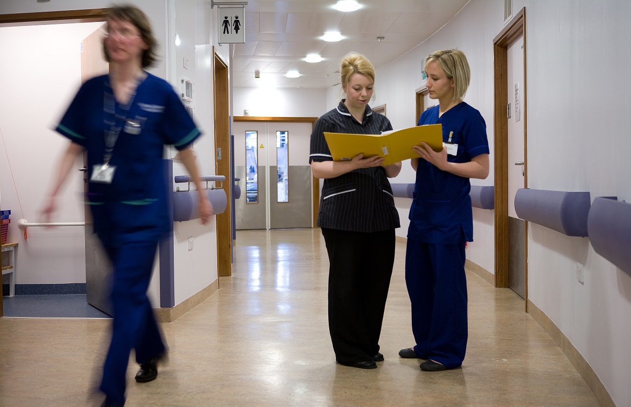 Nurses discuss information in a clipboard folder in a hospital corridor. Communication. Two women. Staff. Hospital environment.