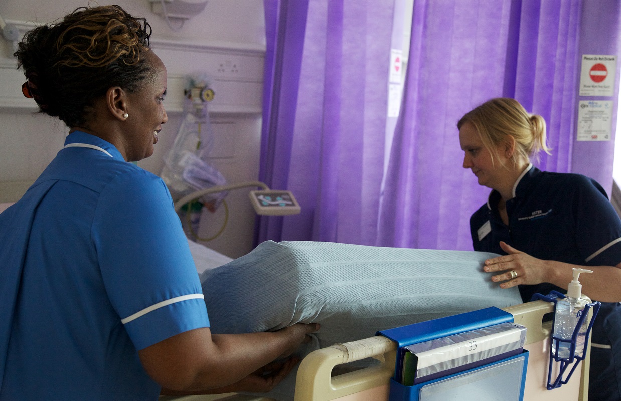 Two nurses work together to change an empty hospital bed