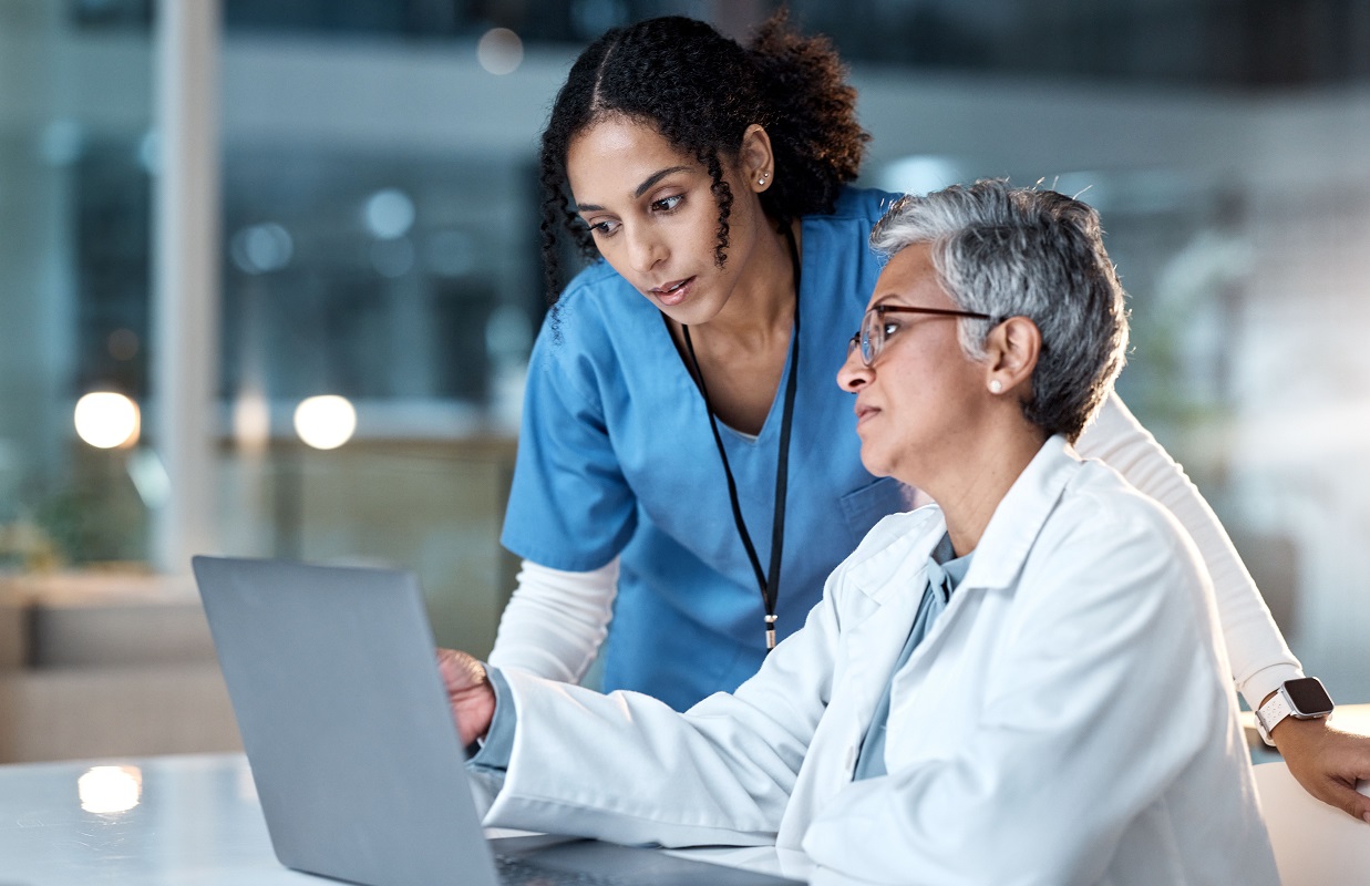 Two female clinicians look at a laptop together