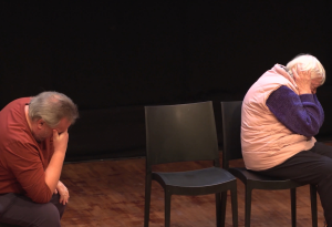 A male and female actor sit on stage with their backs to each other to portray a breaking point in the caring relationship between mother and son.